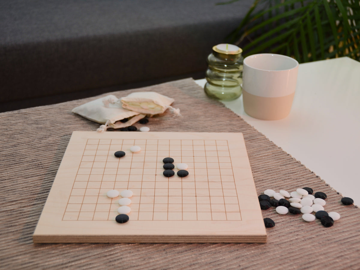 Baduk Holzbrett auf dem Tisch: Seitliche Ansicht des aufgebauten Spiels in wohnlicher Atmosphäre.